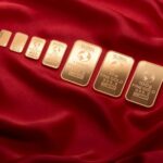 Array of fine gold bars displayed on rich red fabric, symbolizing wealth and luxury.