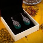 Close-up of silver and green gemstone earrings in a box on vibrant fabric.