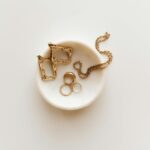 Stylish arrangement of gold jewelry including rings, earrings, and a necklace on a marble dish.